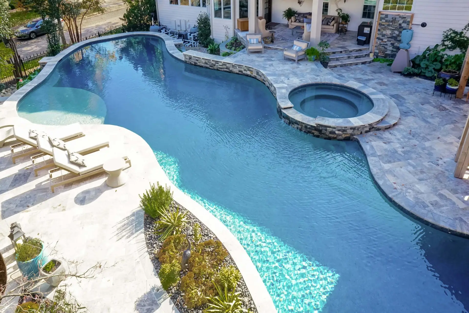 Overhead view of custom luxury freeform pool with tanning ledge, silver travertine, weeping wall, spa and stonework in North Raleigh