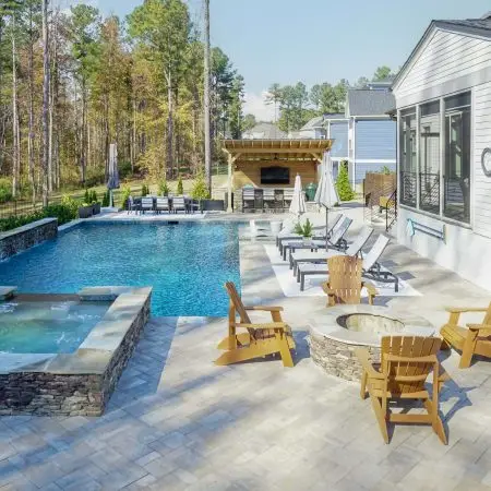 Long view of custom pool with spa, weeping wall, Cambridge pavers, firepit and grill island in Raleigh, NC
