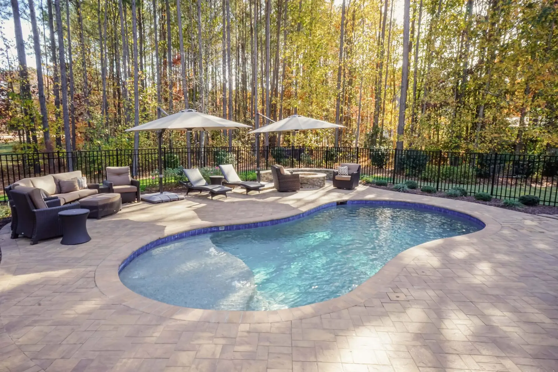 Youngsville NC custom concrete pool with Cambridge pavers, landscaping, fire pit, and seat wall