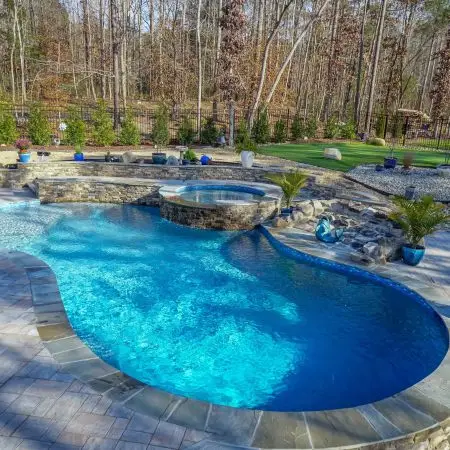 A freeform custom pool and spa in Pittsboro, NC with Cambridge pavers and landscaping.