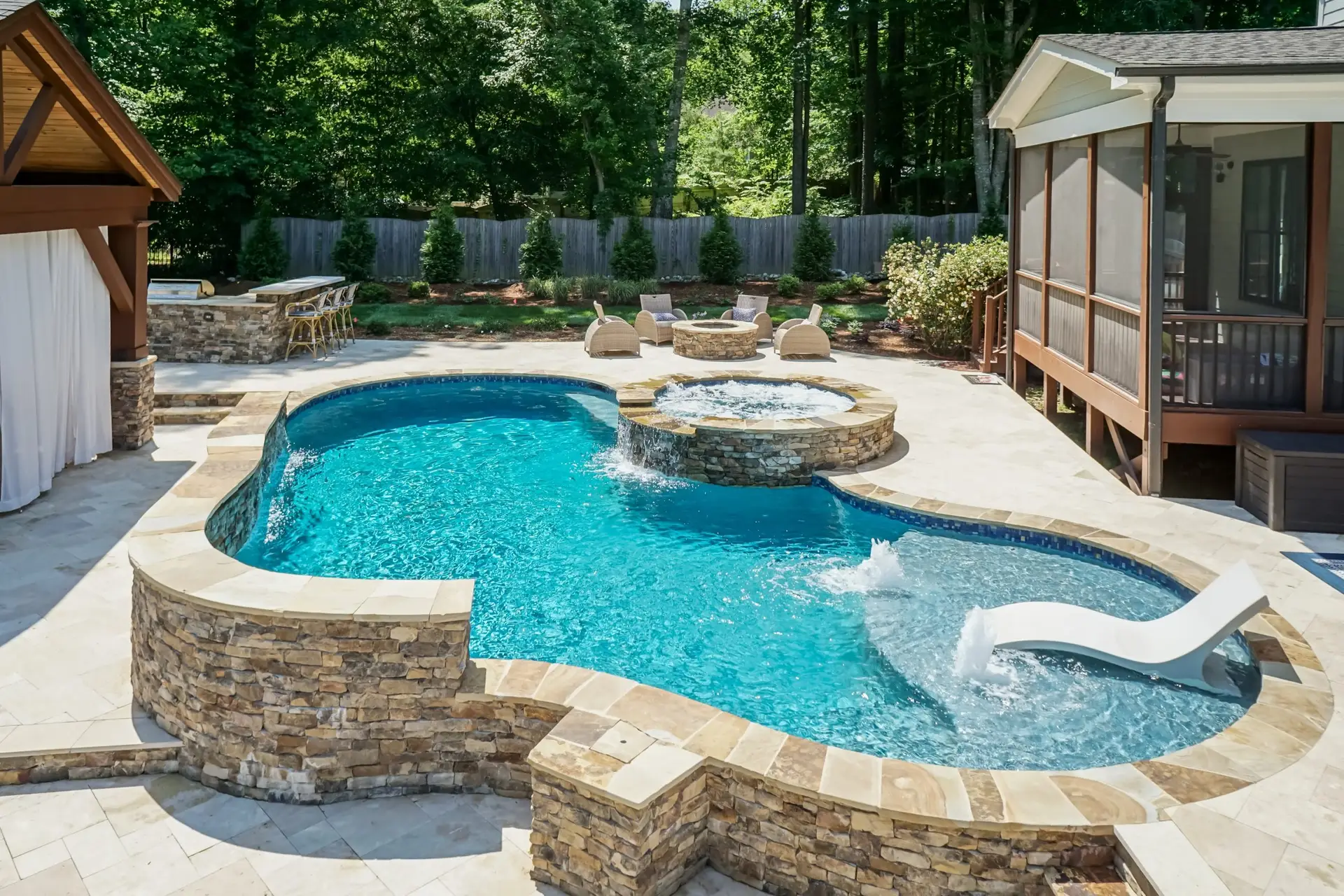 Freeform custom pool with raised spa, tanning ledge, firepit and grill island in Holly Springs, NC