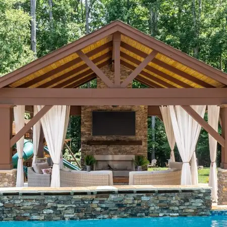 Freeform custom pool with weeping wall, pavilion, grill island, and firelace in Holly Springs, NC backyard.